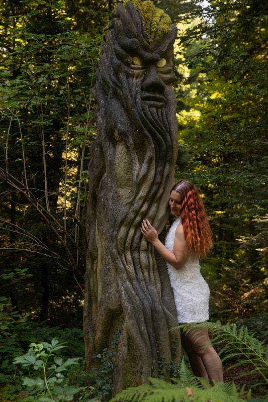 Foto einer jungen Frau mit roten, lockigen Haaren und einem weissen Kleid. Sie steht neben einer Skulptur