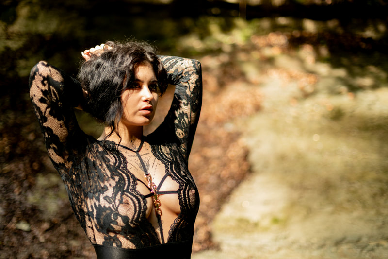 Foto einer jungen Frau mit schwarzen Haaren und Tattoos in einem schwarzen, durchsichtigen Tüll- Oberteil